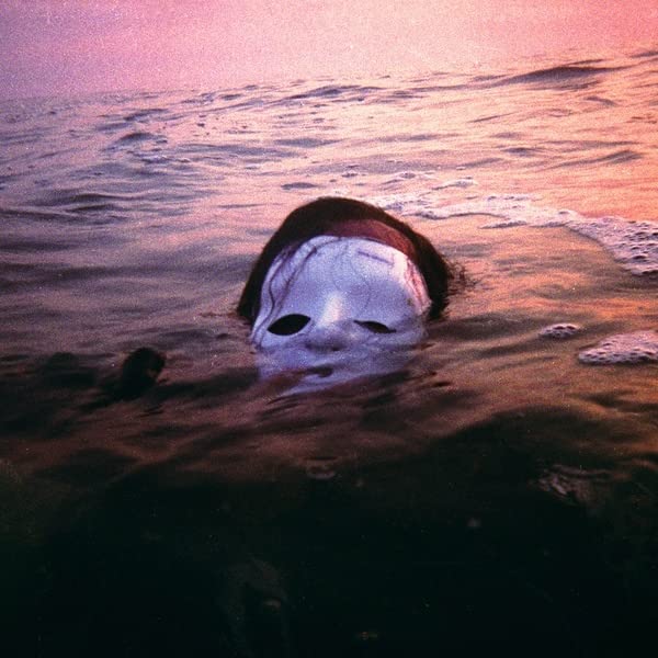 Masked face partially submerged in ocean water at sunset.