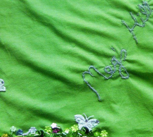 The image shows a green fabric with embroidered flowers. Alt text: Green fabric with embroidered flowers along the bottom edge.