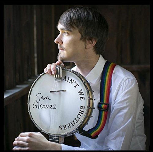 Man holding banjo with "Sam Gleaves" and "Ain't We Brothers" written on it.