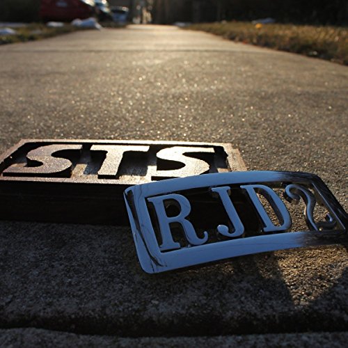 "Metal plates with 'STS' and 'RJD2' on a road curb, with a road behind."