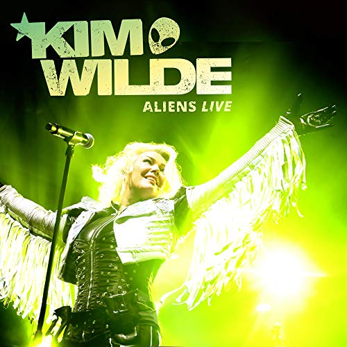 Kim Wilde on stage, arms outstretched, wearing fringe costume, under bright green and yellow lights.