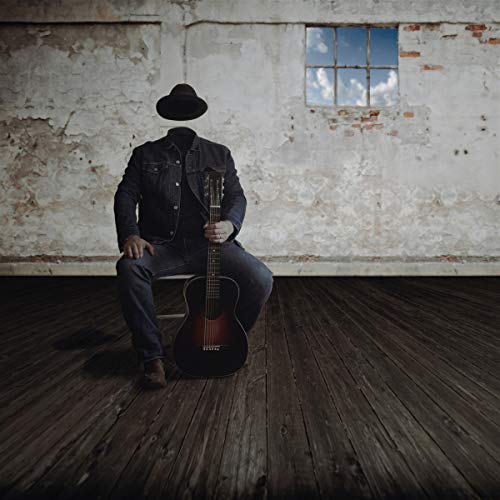 Man with no face sits playing an acoustic guitar indoors.