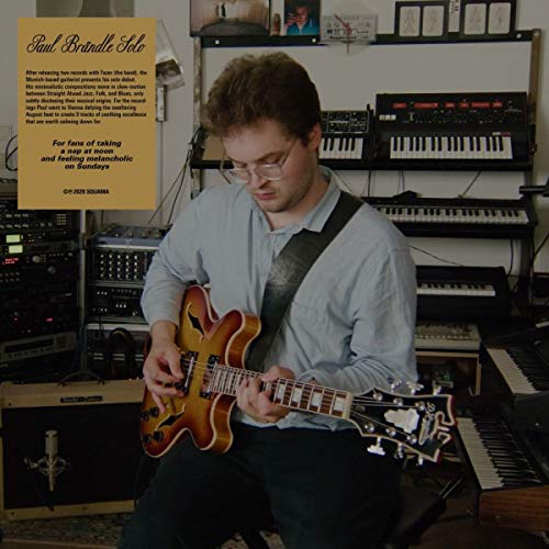 Man playing electric guitar in a room with keyboards and audio equipment.