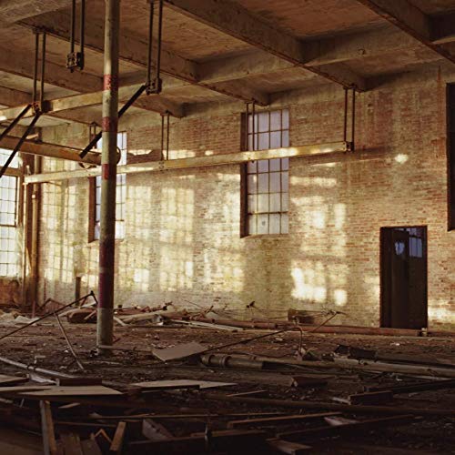 Brick interior with sunlight streaming through large windows, debris on floor.