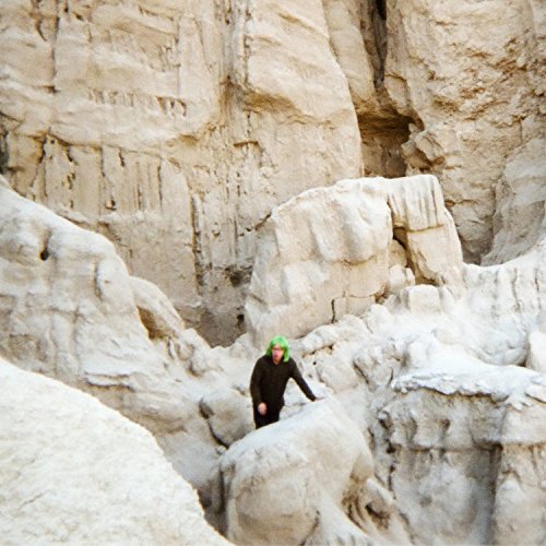 A person in a green helmet and black clothing climbs rugged, white rocky terrain.