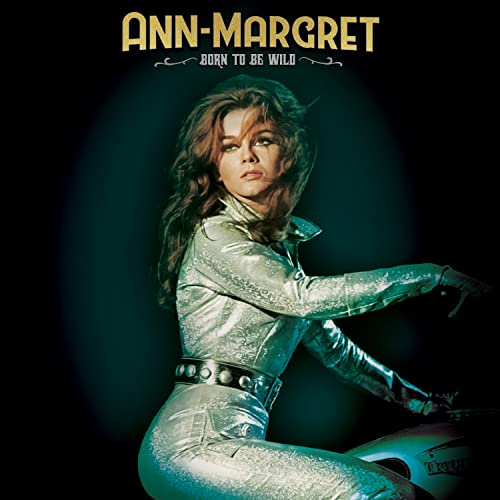 Ann-Margret in a silver jumpsuit, looking over her shoulder on a motorcycle.