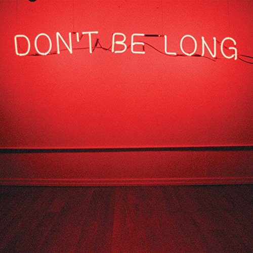 "Red wall with neon sign reading 'Don't Be Long' on wooden floor."