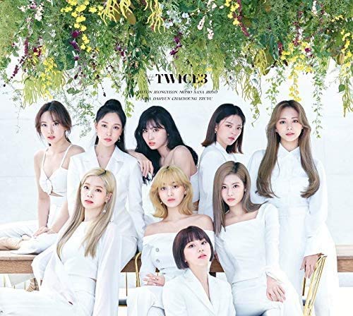 Nine women in white clothing pose amongst lush green foliage.