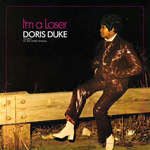 Doris Duke sits on a wooden guardrail in a dark jacket and white boots.