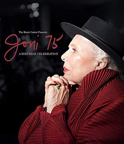 Joni Mitchell in a red shirt and black hat, looking downward.