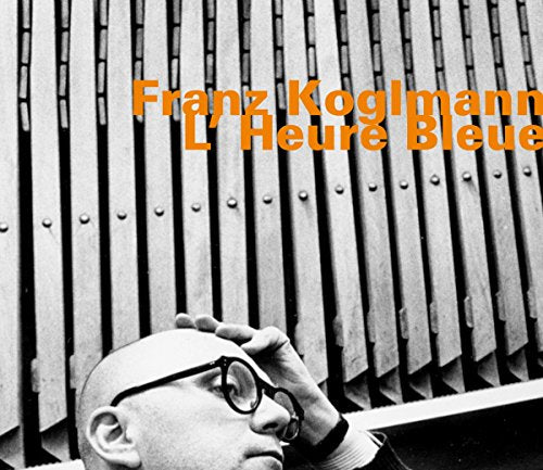 Bald man in glasses touches his head, in front of metal slats, with orange text overlay.
