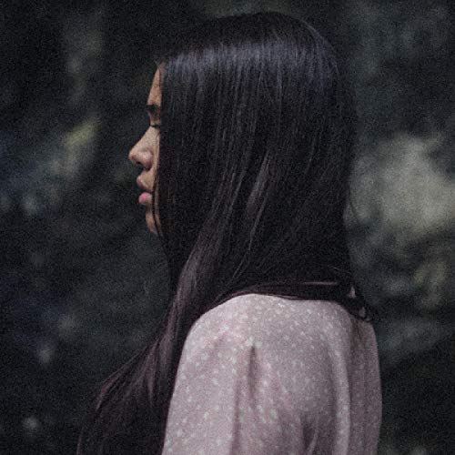 A woman with long dark hair wearing a pink dotted blouse is shown in profile.