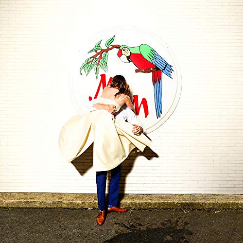 A man holding a woman in a white dress against a white brick wall with a parrot logo.
