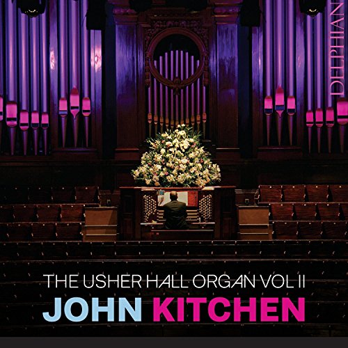 Organist playing at an organ surrounded by flowers, in a dimly lit concert hall.