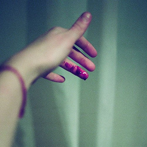 A hand with red, glossy nails is reaching out against a dark green background.