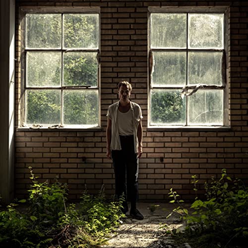 Man standing between two large windows in a brick room.