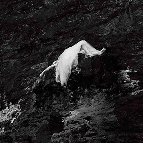 Black and white image of a person in white clothing on rocks.