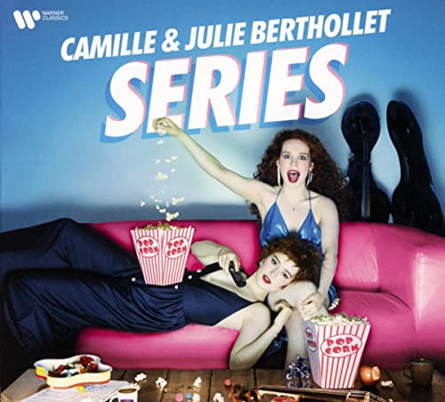Two women in blue dresses lounge on a pink couch with popcorn.