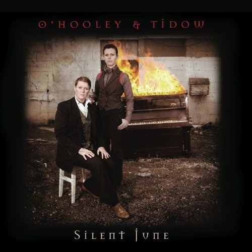 "Album cover featuring two men beside a burning piano in a grimy room."