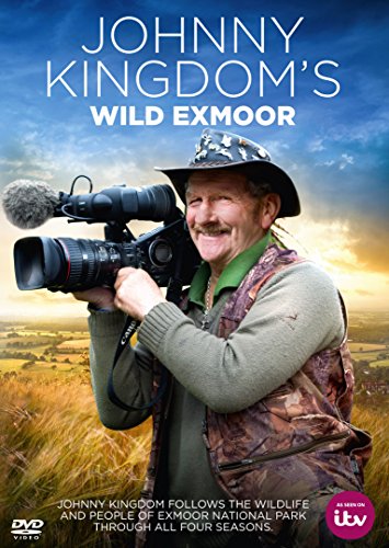 Johnny Kingdom wearing a hat and holding a video camera in a grassy field.