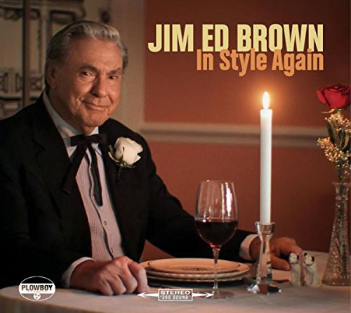 Man in a tuxedo sits at a table with a lit candle.
