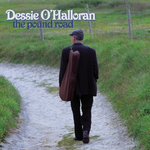 Man in black suit and cap walks down a dirt path with a guitar case.