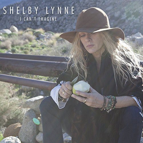 Shelby Lynne sits with a pear and knife, wearing a brown hat.