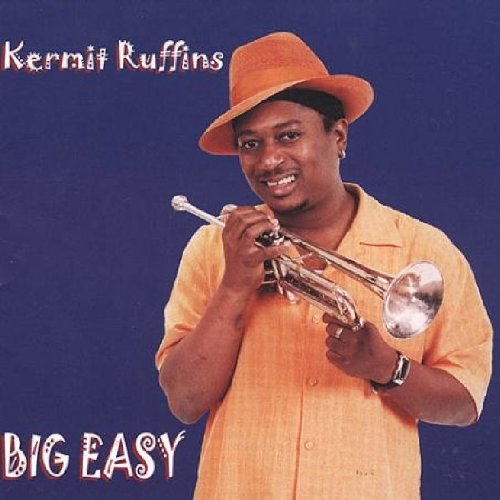 Man in yellow shirt and hat holding trumpet, against a blue background.