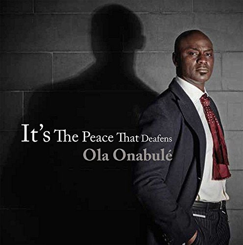 Man in suit and red tie stands beside his shadow on a grey brick wall.