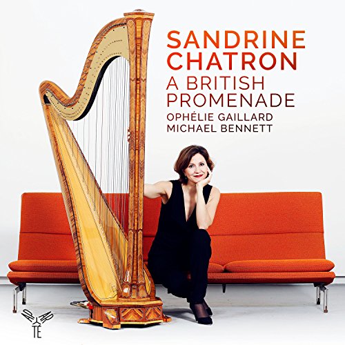 Woman sitting beside a large golden harp on an orange sofa.
