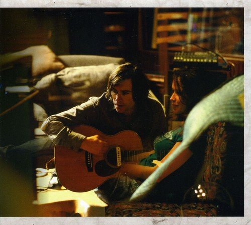 "Album cover with a man playing guitar in a dimly lit, cluttered room."
