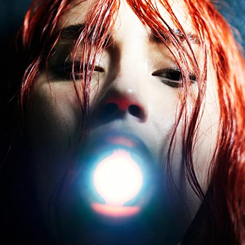 Close-up of a woman with red hair and a bright light emanating from her mouth.