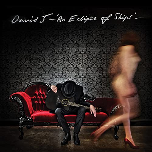 CD cover: man with guitar and blurred figure on ornate couch.