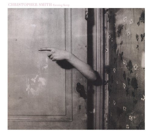 "Album cover featuring a black and white image of a hand reaching through a door."