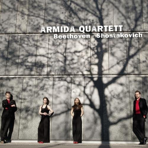 "CD cover featuring four musicians in formal attire against a grey wall with tree shadows."