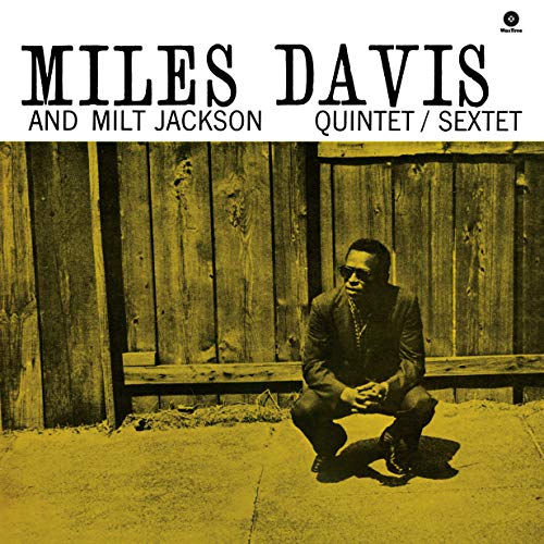 Miles Davis crouching in front of a wooden fence on a yellow-toned album cover.