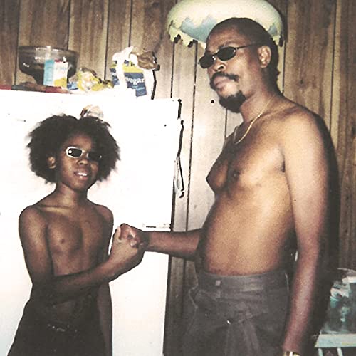 Vintage photo of two shirtless Black men with sunglasses, holding hands.