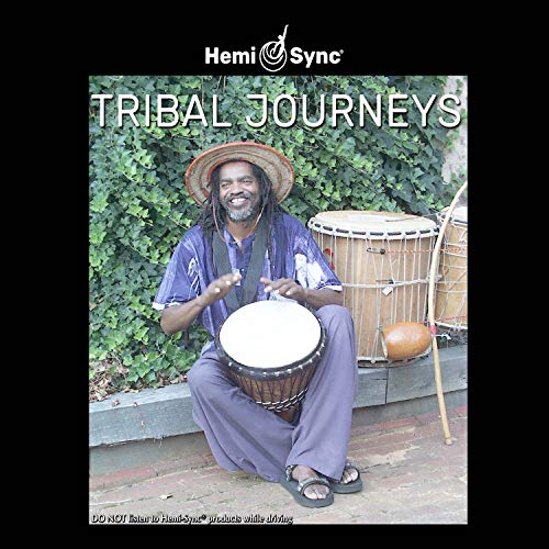 Man sitting on ground playing djembe drum, surrounded by other drums and greenery.