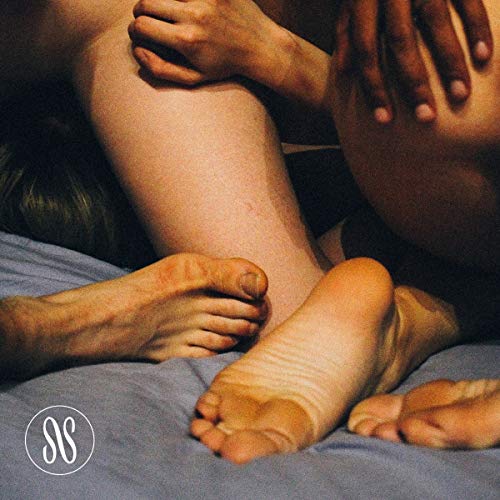A close-up image of intertwined feet and hands on a blue fabric background.