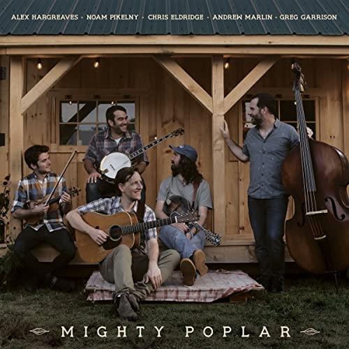 Five musicians with string instruments pose in front of a small wooden building.