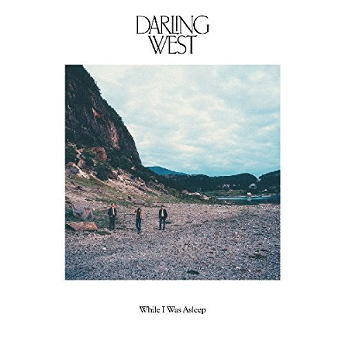 The alt text for the image is: "Album cover with three men standing on a rocky beach."