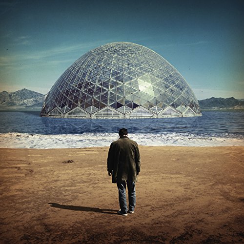 Man standing on beach, facing large geodesic dome over water.