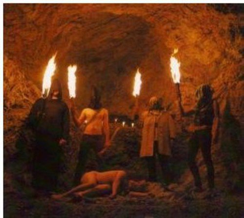 Group holding torches in a dark, cavernous space; one figure is prone.