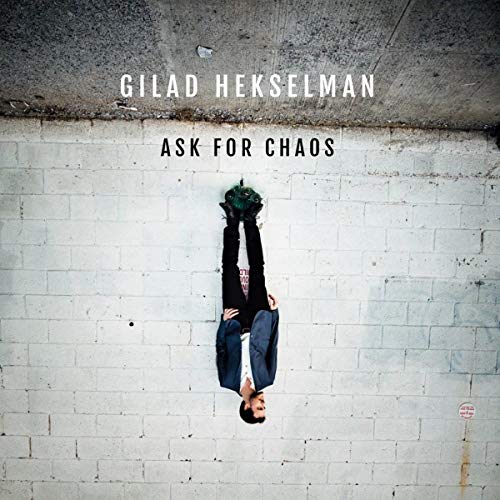 "Album cover with a man hanging upside down against a white brick wall."