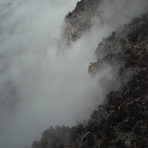 The image depicts a rocky cliffside shrouded in fog. For accessibility purposes, a concise alt text could be: "Foggy rocky cliffside with dark vegetation."