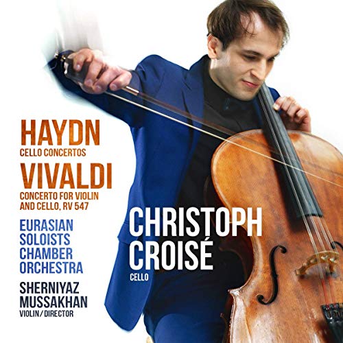 A man in a blue suit holds a cello against a white background.