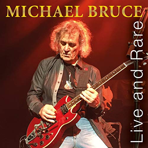 Michael Bruce playing a red electric guitar on stage.
