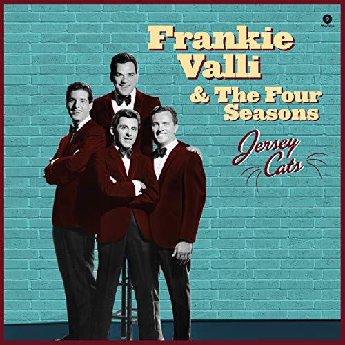 Frankie Valli and The Four Seasons in suits against a blue brick wall background.