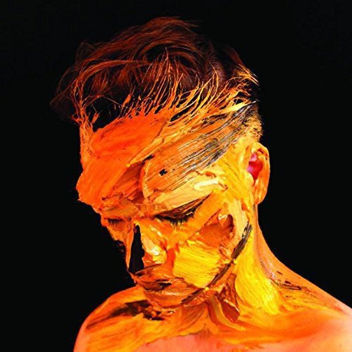 "Man with brown hair and orange paint covering his face against a black background."