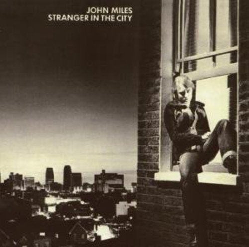 "Album cover: man sitting on a windowsill, cityscape in the background, sepia tone."